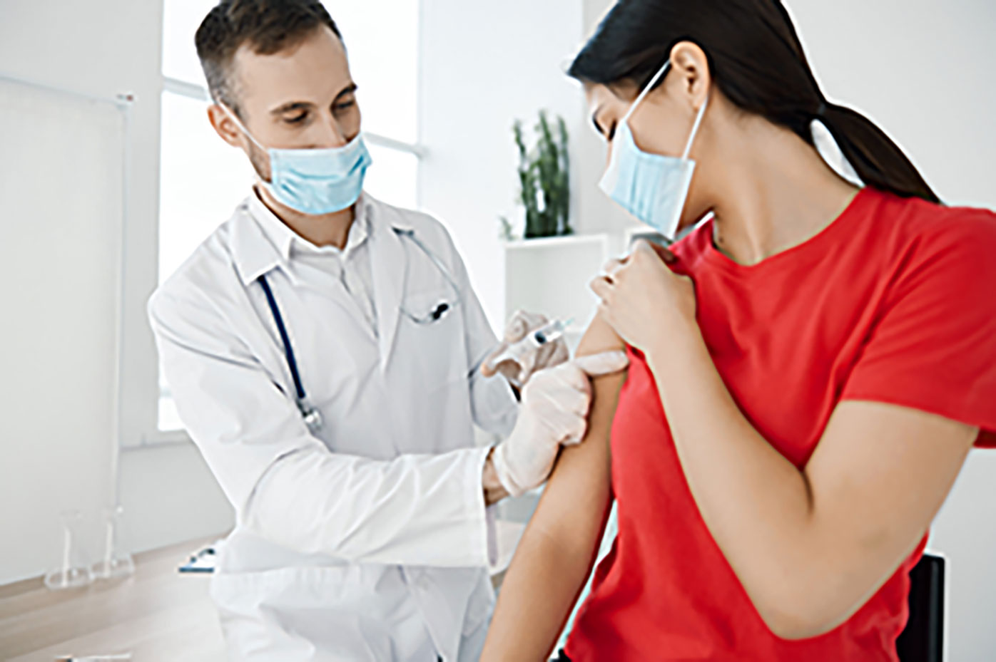 Doctor in mask administering shot  to woman in mask.