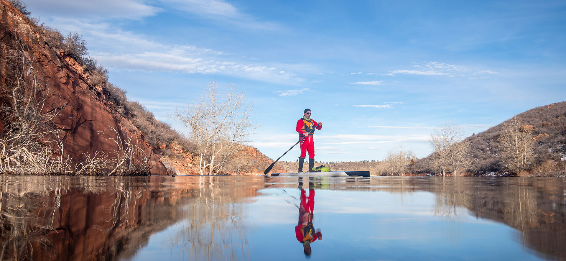 Man paddle boarding with a red water suite on.