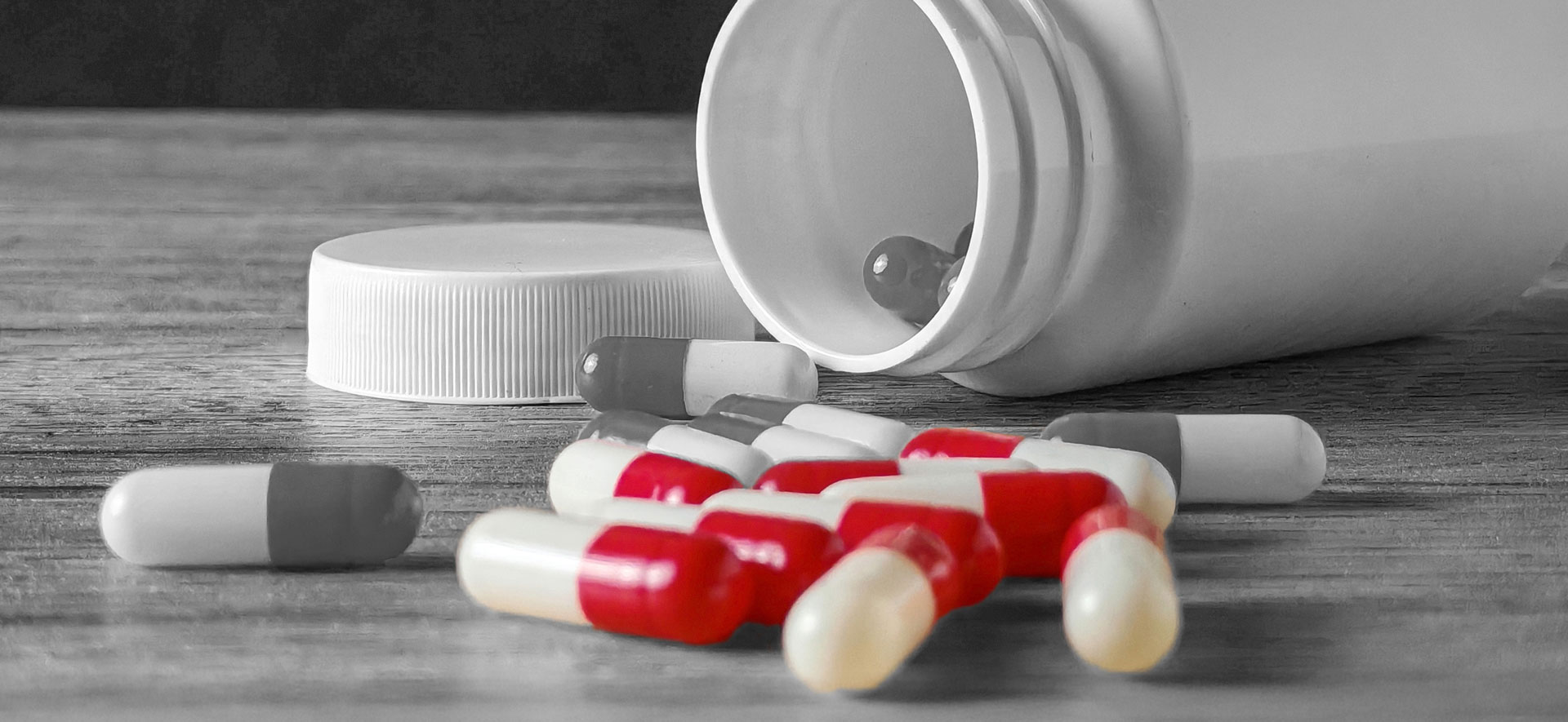 A tumbled bottle reveals bright red opioid pills scattered across a cool gray table surface