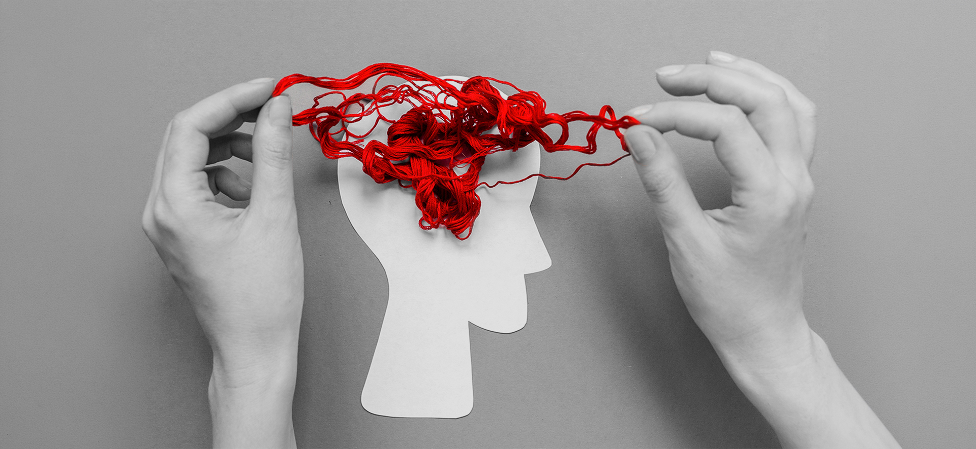 Hands pulling apart tangled red yarn inside the silhouette of a human head, symbolizing cognitive decline associated with Alzheimer’s disease.