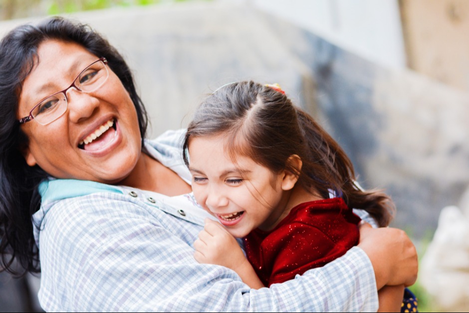 A mother joyfully laughs, hugging her daughter
