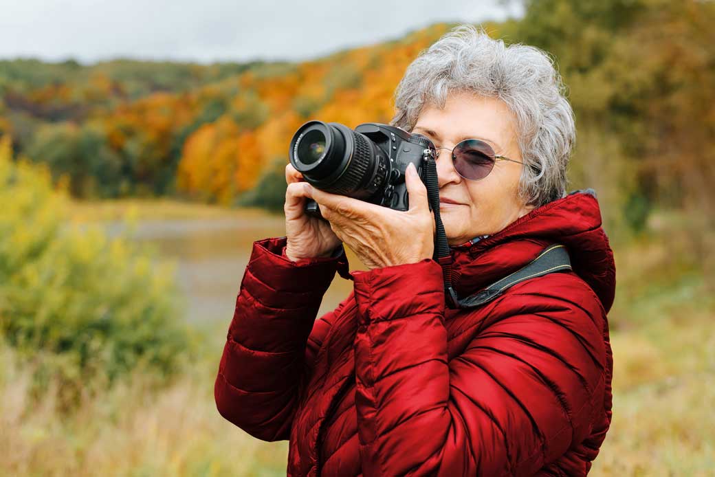 An older birdwatcher in a park points her camera and gazes into the distance