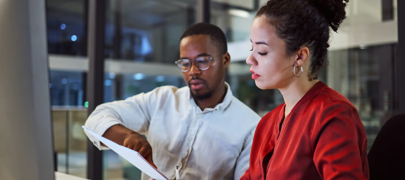 A woman in a red shirt and a many in a white shirt study a paper.