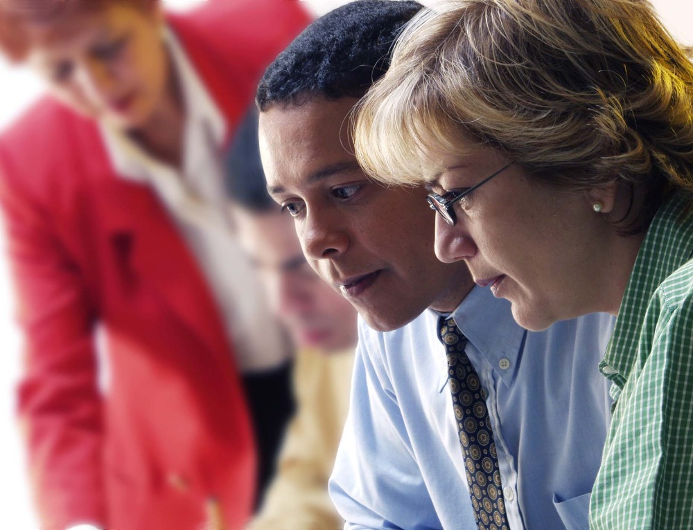 Colleagues lean in close to study a document together, one in red at the edge of the frame — the shared scrutiny that precedes a landmark in-force transaction