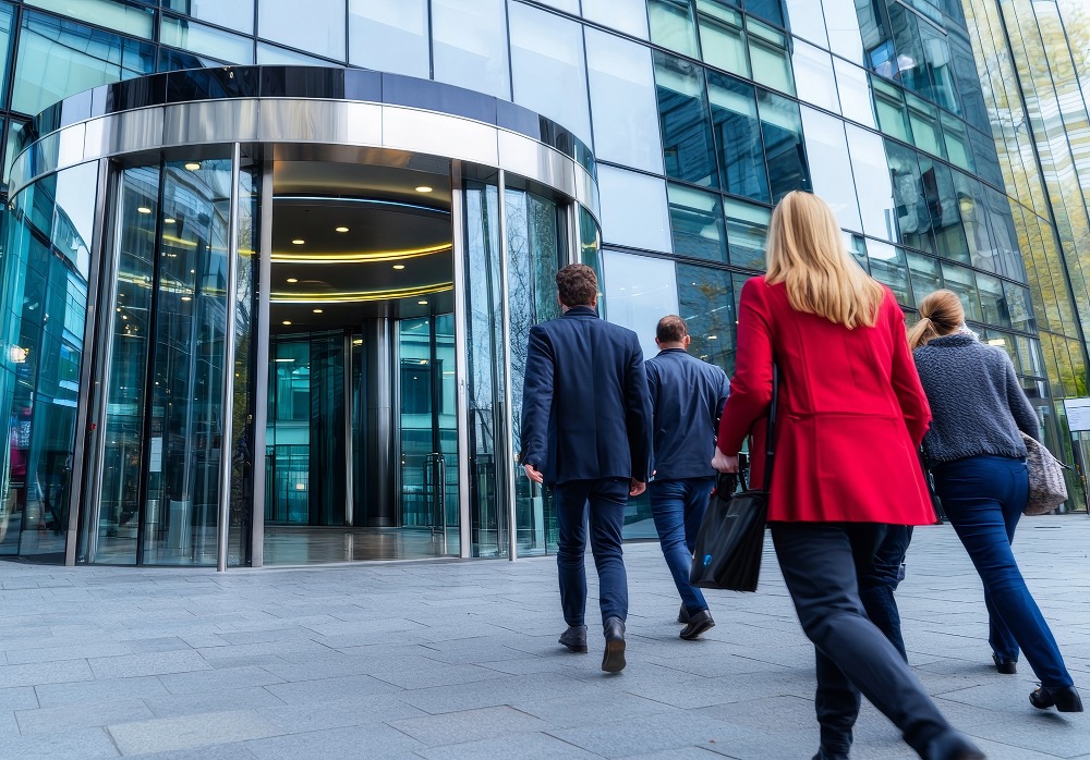 A group of workers busily march toward the revolving door of a corporate tower