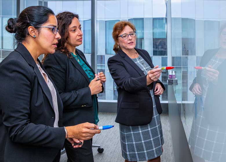 A trio of physicians at RGA stand before a whiteboard, discussing a medical underwriting case.