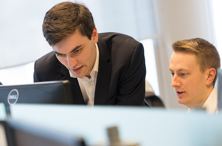 A pair of colleagues meet over trading screens