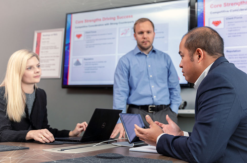 A group of colleagues meet before a banner reading core strengths drive progress