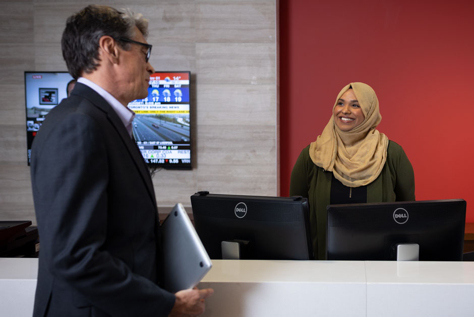 A businessman and businesswoman in a hijab converse across a desk