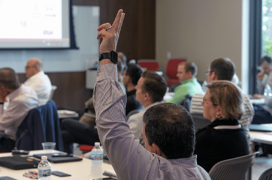 A participant raises a hand to question a presenter