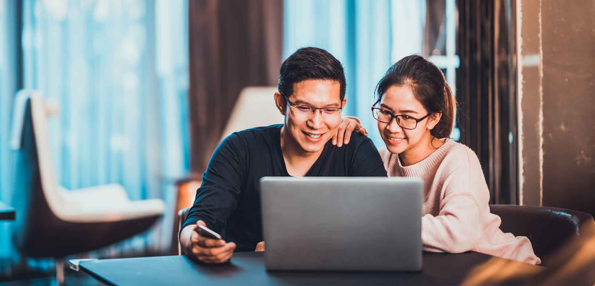 An Asian couple sits together looking at a laptop and smiling