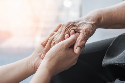 An elderly individual holds a caregiver's hand