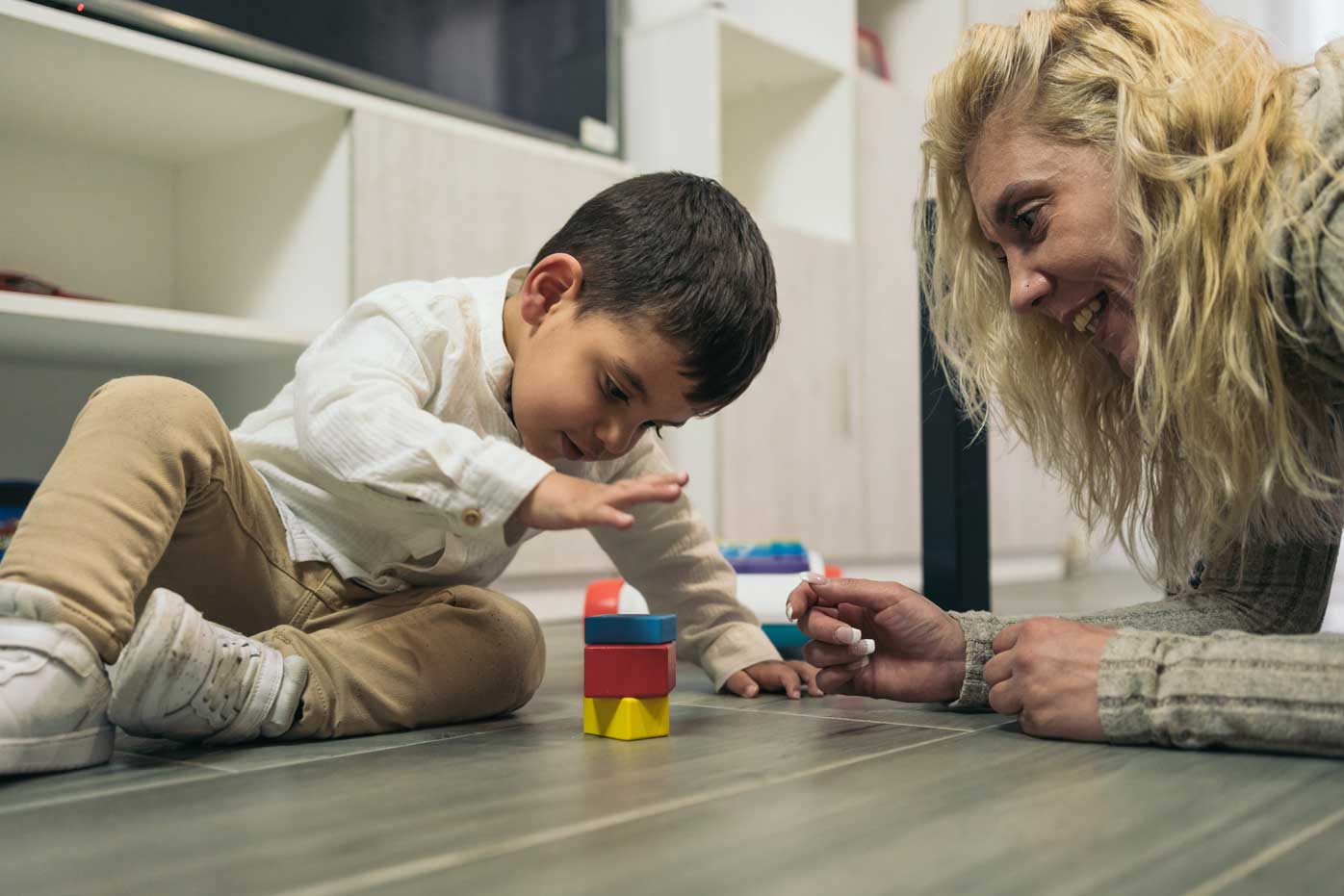 A young child plays with blocks beside his mother