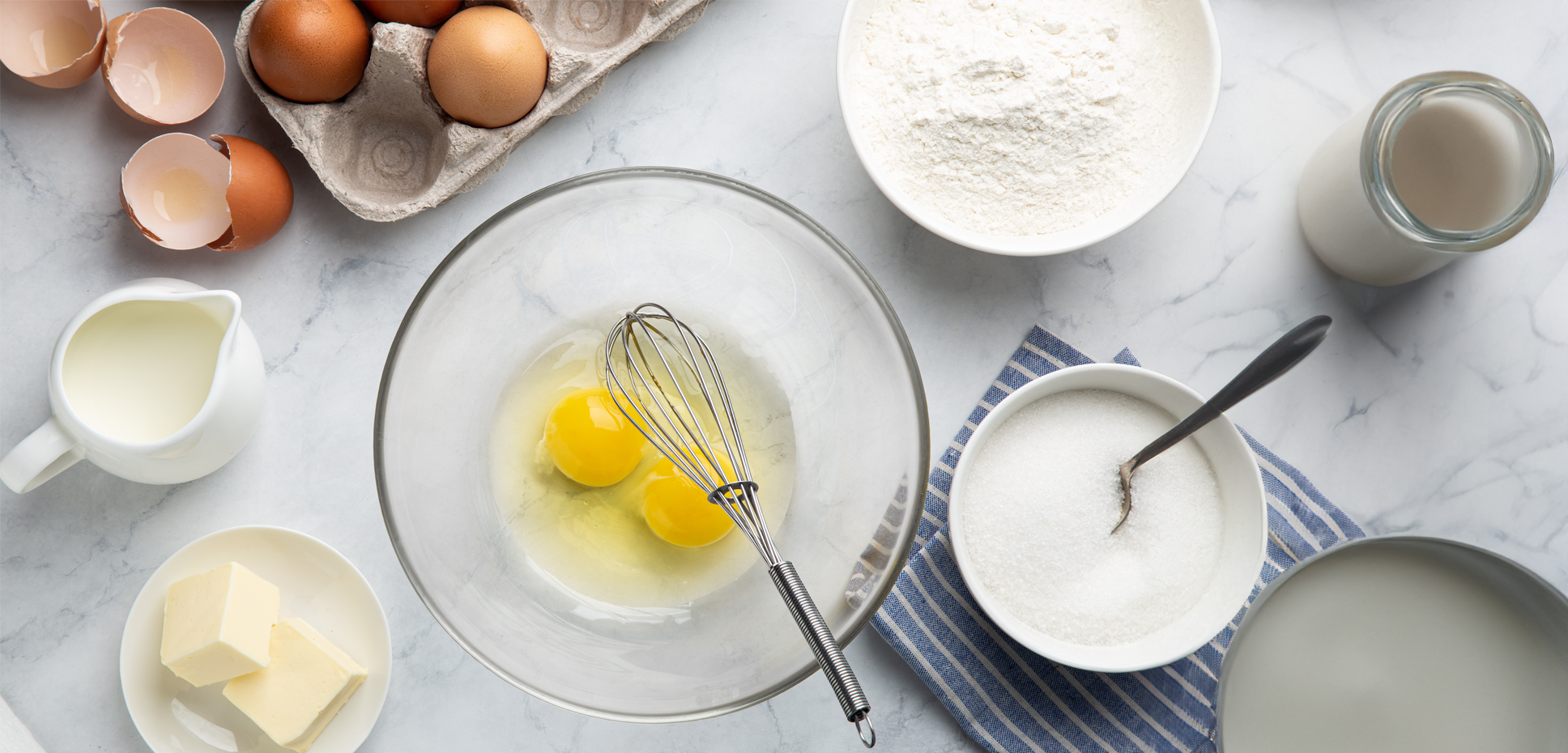 Overhead image of countertop filled with baking items, including eggs, butter, and milk