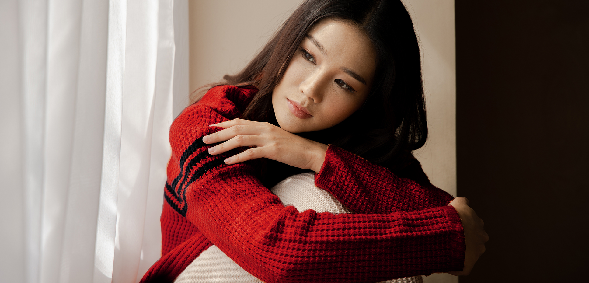 Asian woman in a red sweater looking out the window