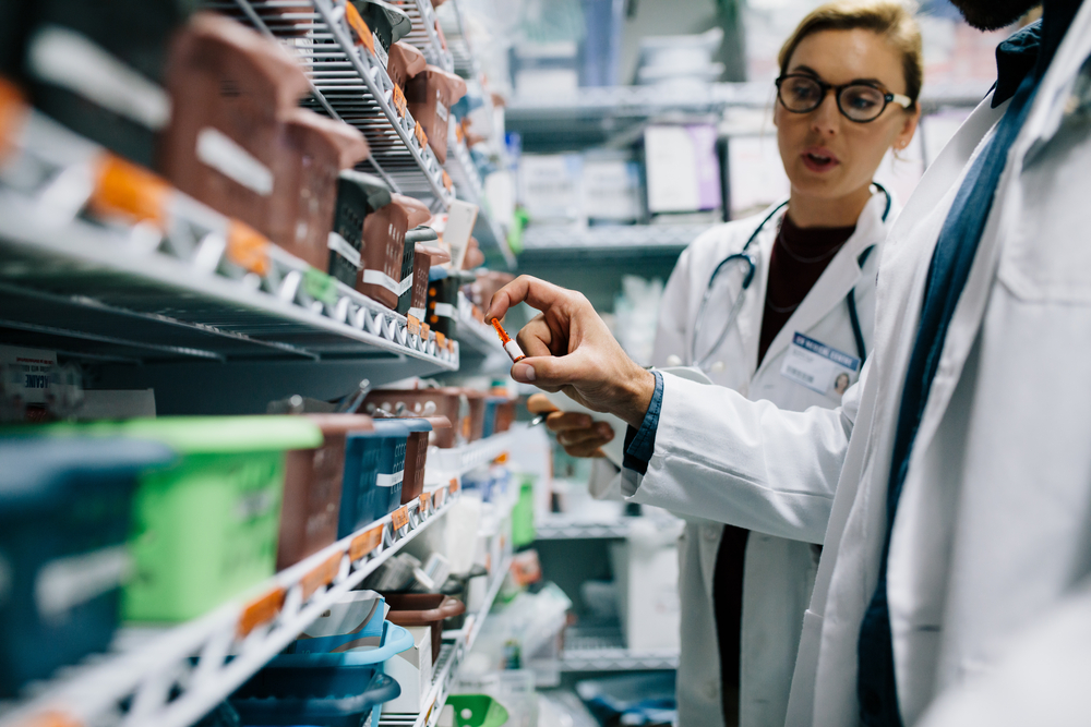 A coated pharmacist looks through shelves for a drug