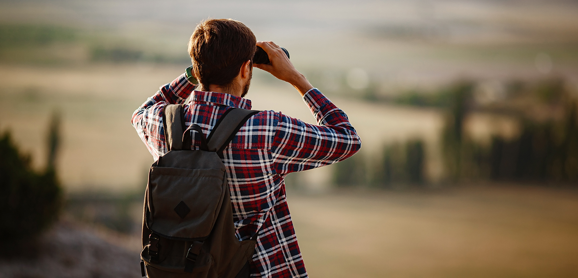 Man in plaid shirt with binoculars looks into the distance