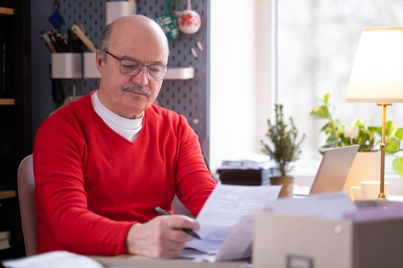 A man wearing a red sweater stares grimly at a stack of forms