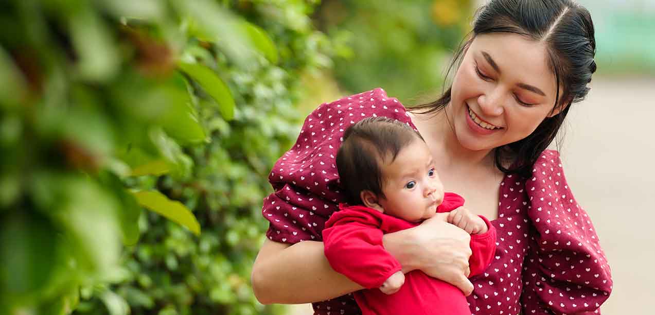 Asian woman in red dress holding baby outside
