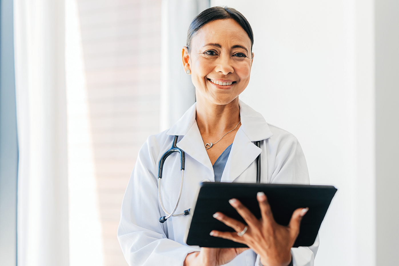 A female physician in a labcoat clutches an ipad