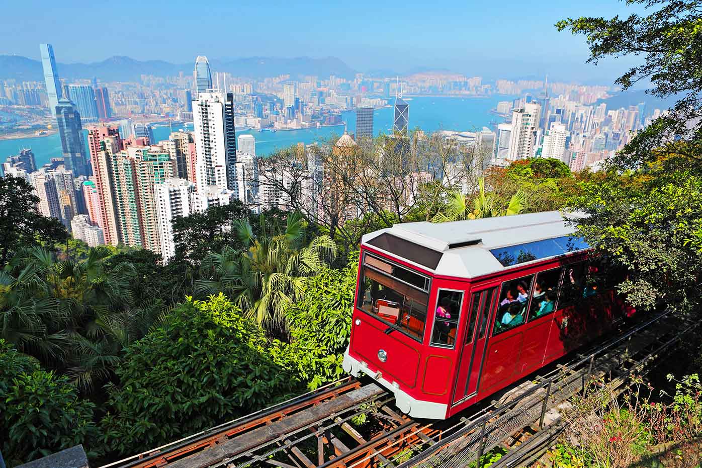 A red tram car ascends to The Peak with a view of Hong Kong and the harbor below.
