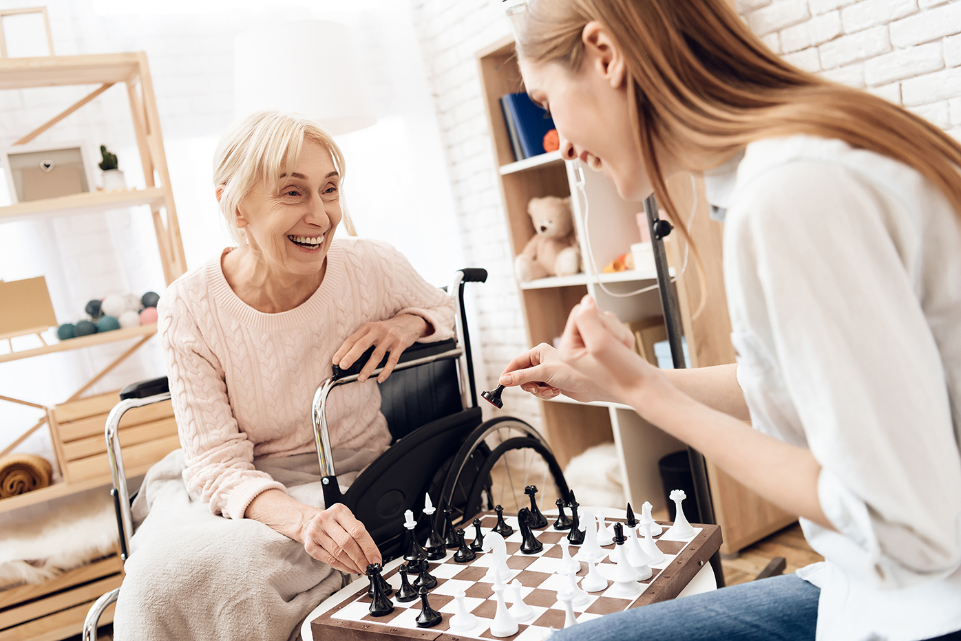 Senior woman playing chess with nurse at care center