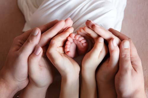 Multigenerational hands clustered around newborn's feet