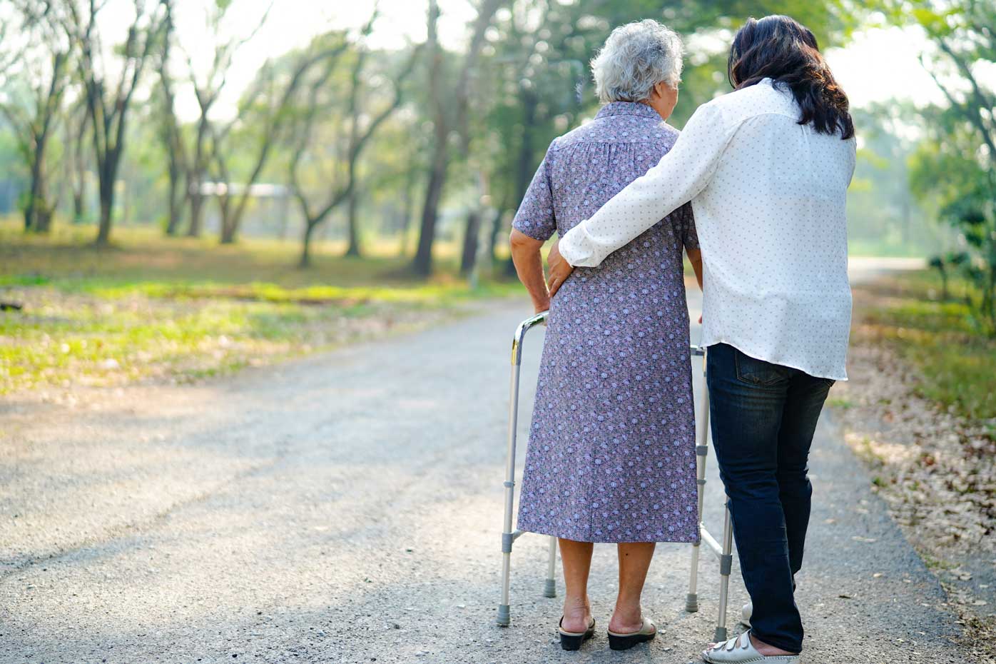 A caregiver and an elderly woman walk in the park