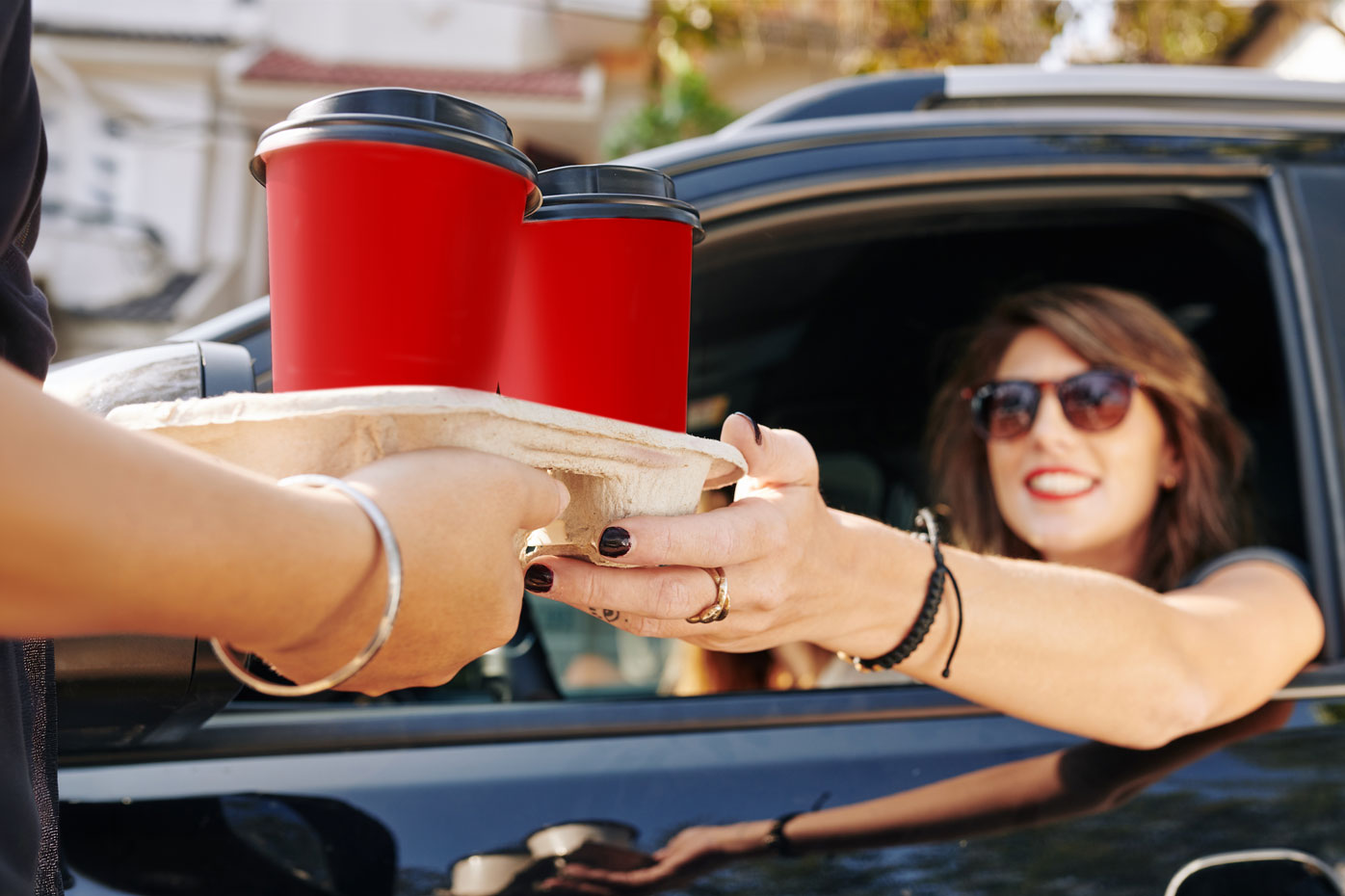A woman in her car takes a tray of red coffee cups 'to go'
