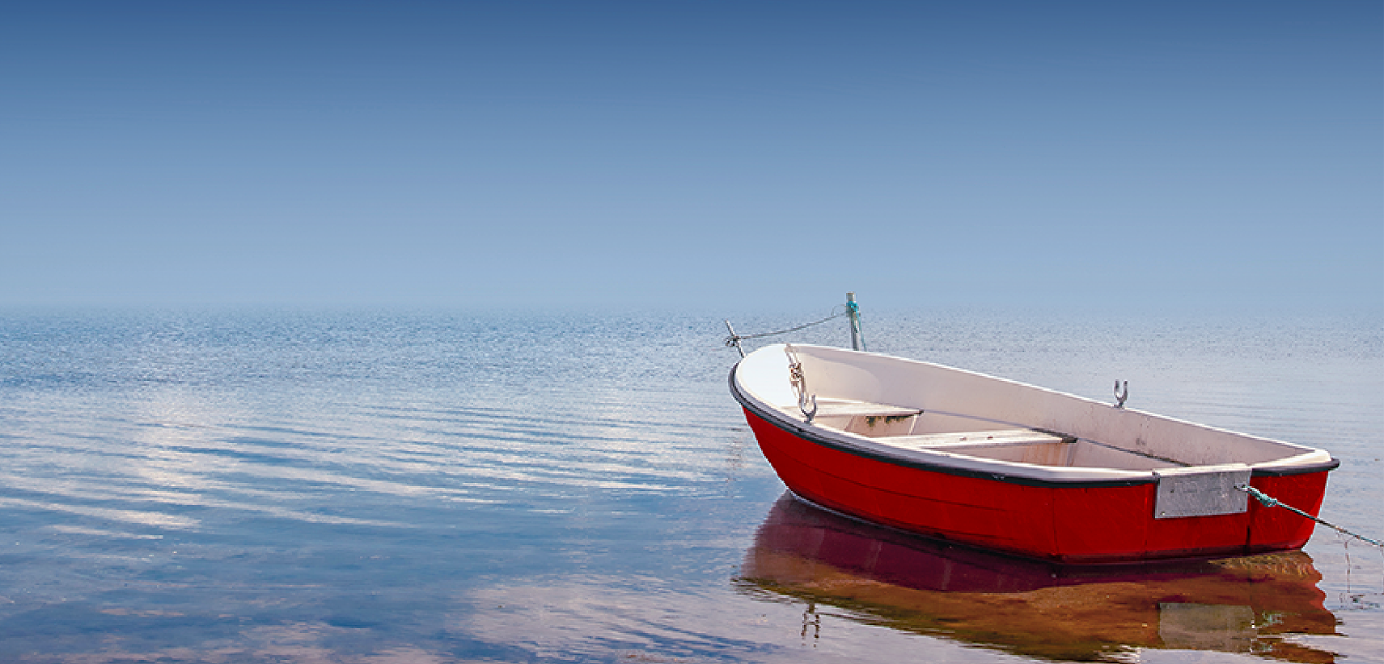A red hulled boat floats out into a calm sea