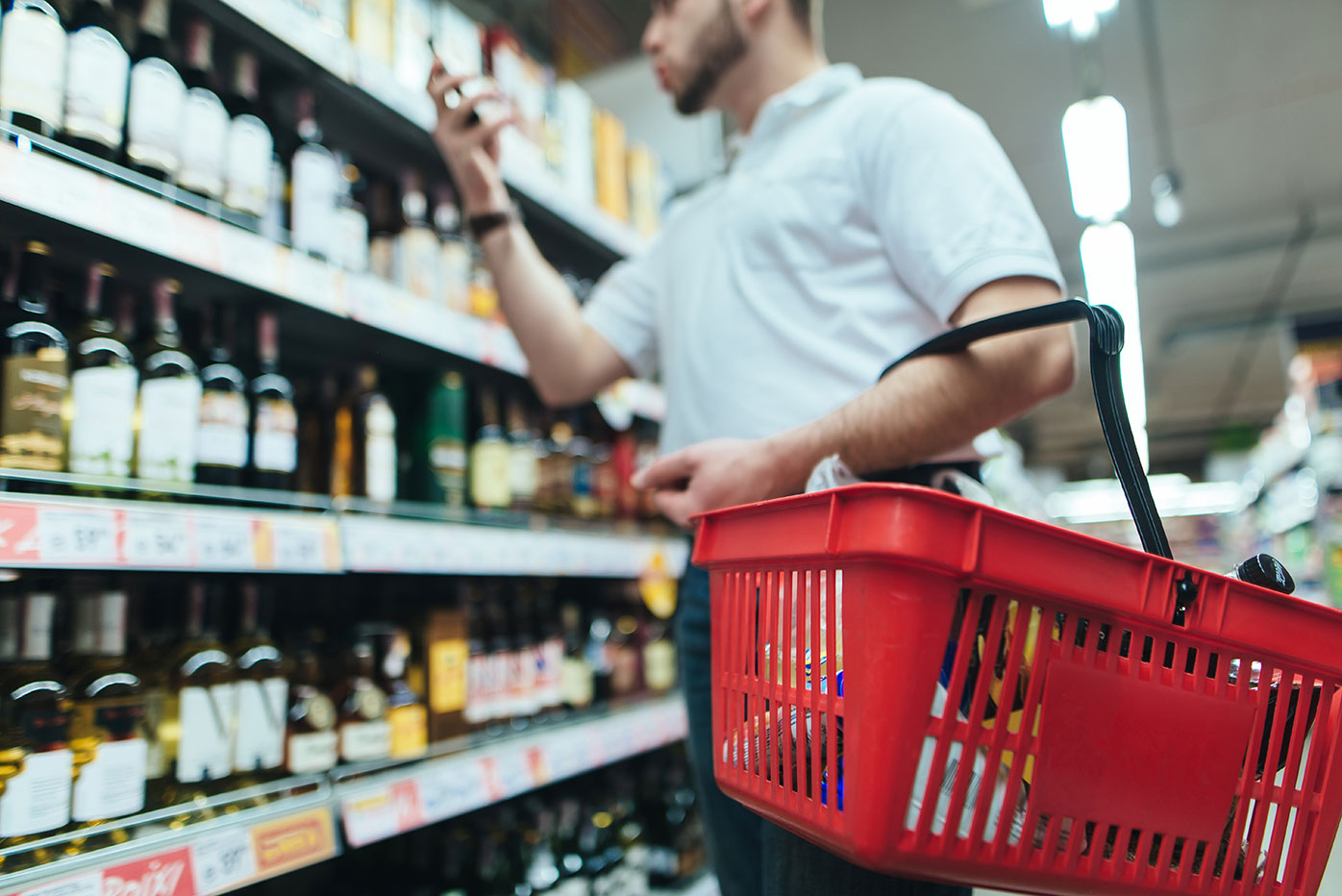 A man shopping for alcohol with a red basket