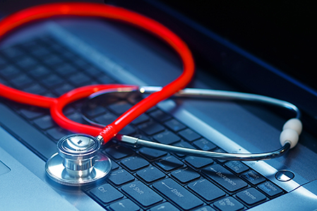 Red stethoscope laying on laptop keyboard
