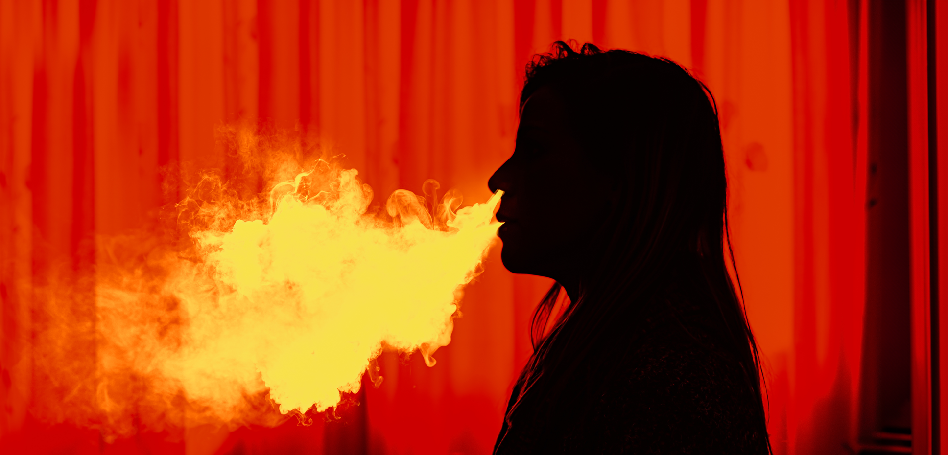 Silhouette of a woman exhaling vape smoke against a red background