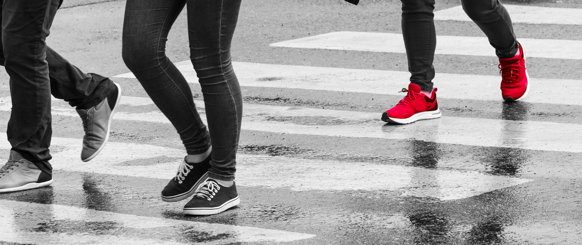Black and white crosswolk photo showing people from the waist down with one pair of shoes in red