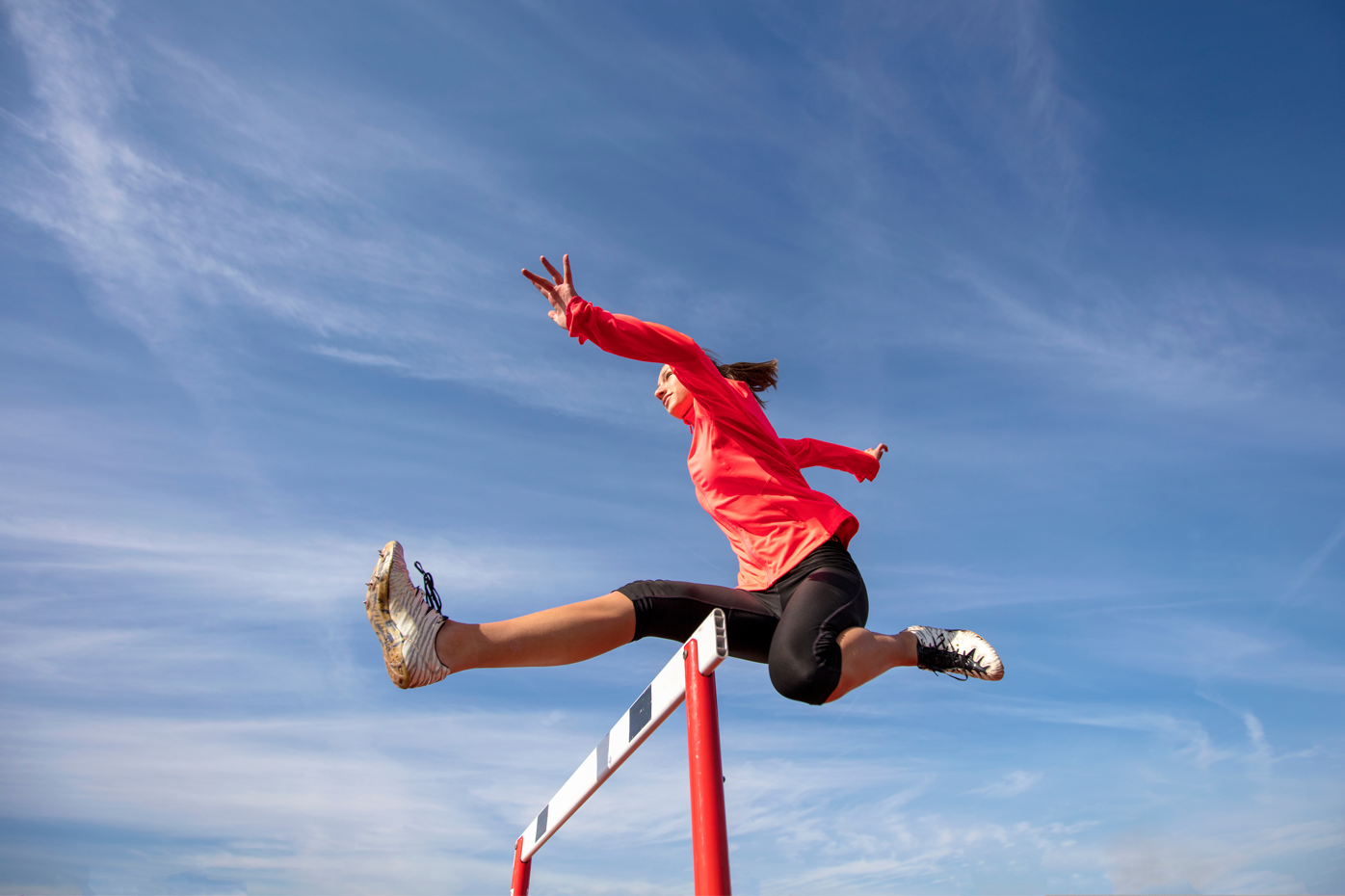 A female athlete soars over a single hurdle