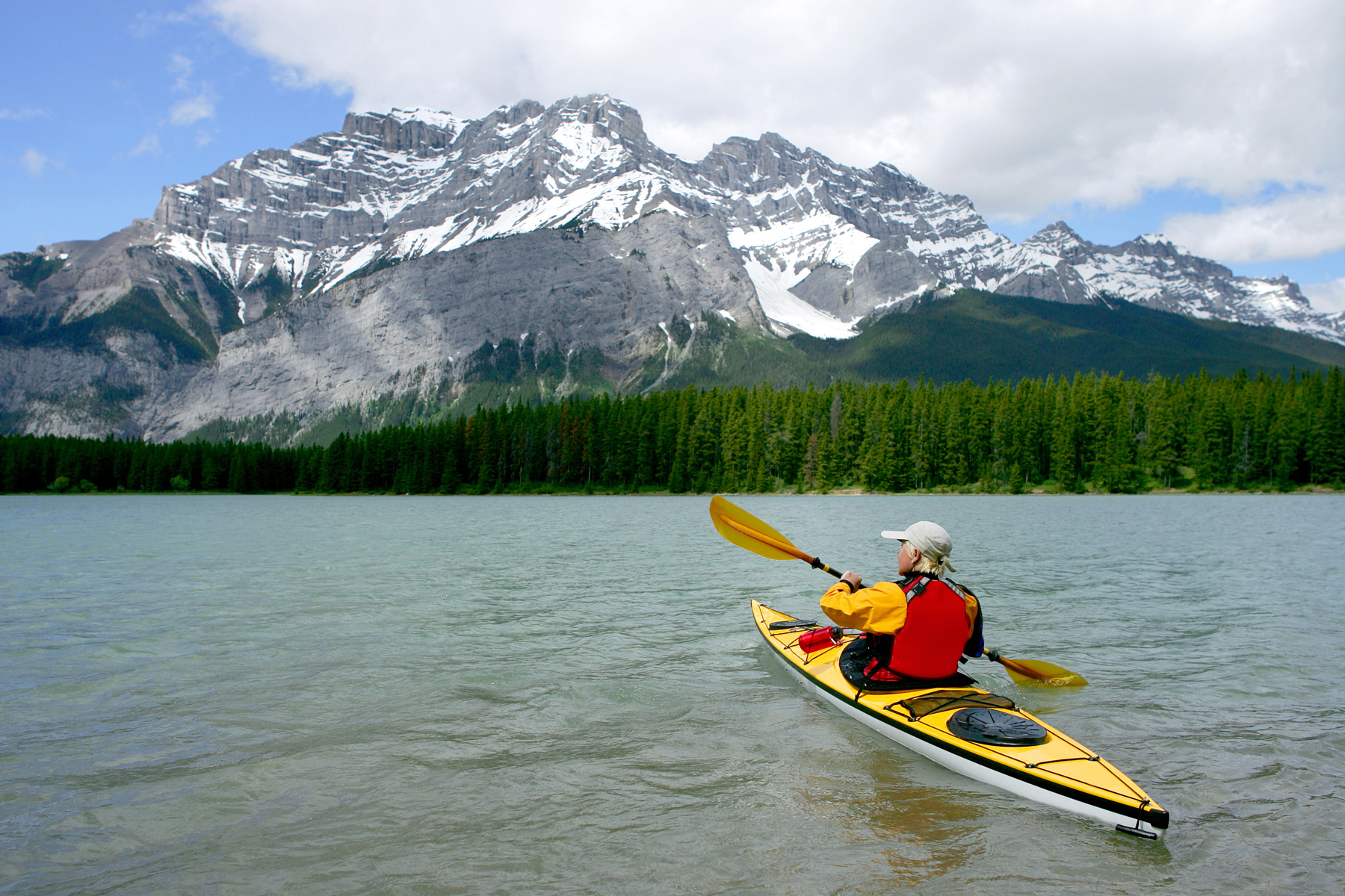 Person in kayak in Canada rowing across a lake toward a snow-capped mountain