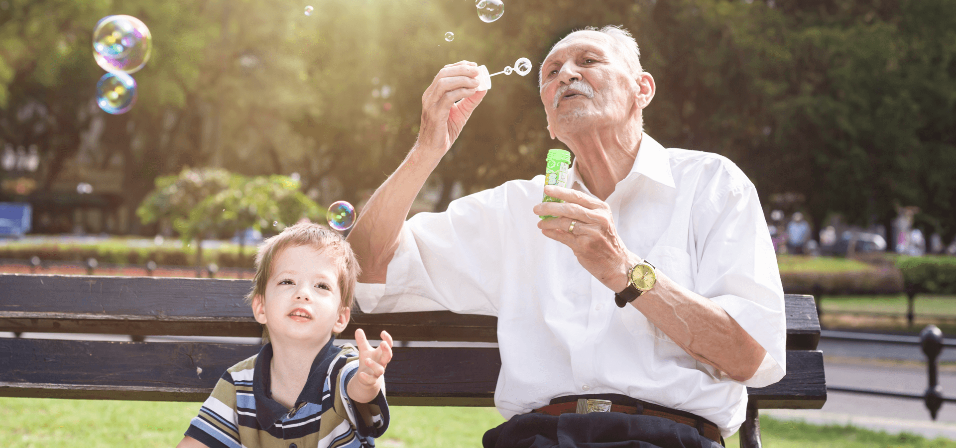 Grandfather Blowing Bubbles on Bench with Grandson