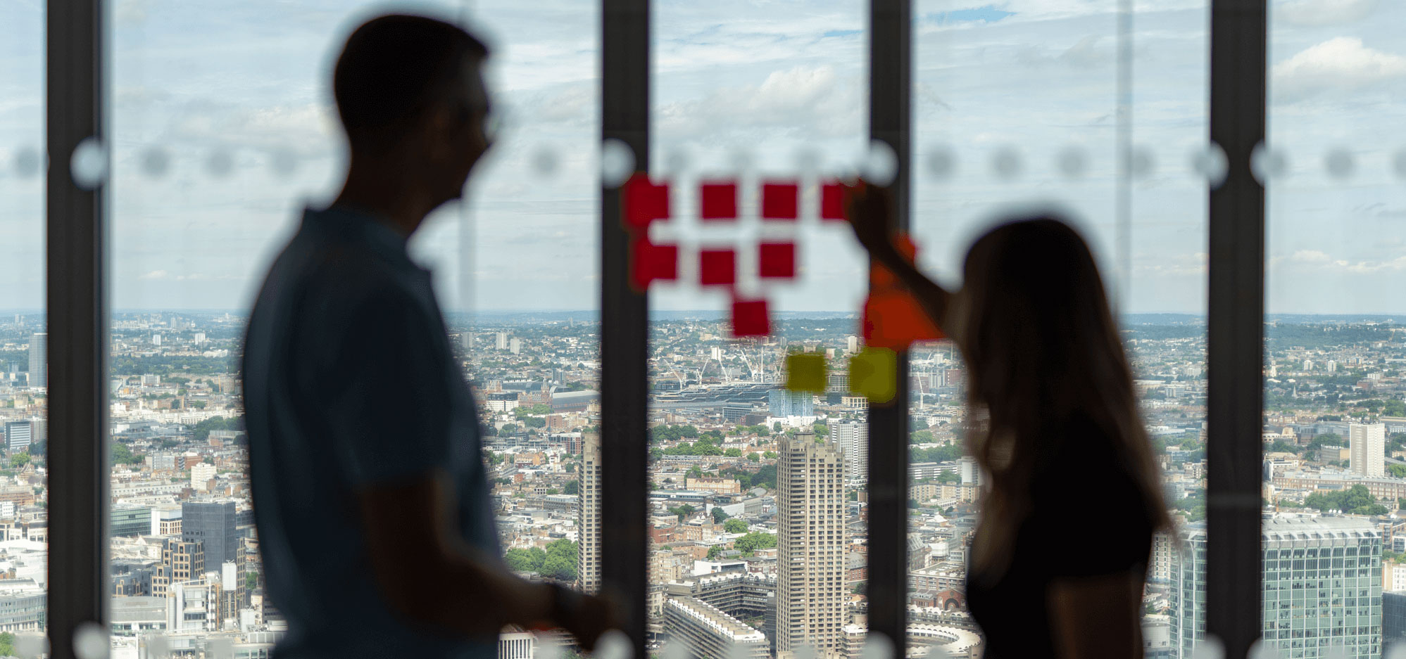 A pair of employees brainstorm new product ideas with sticky notes against glass wall