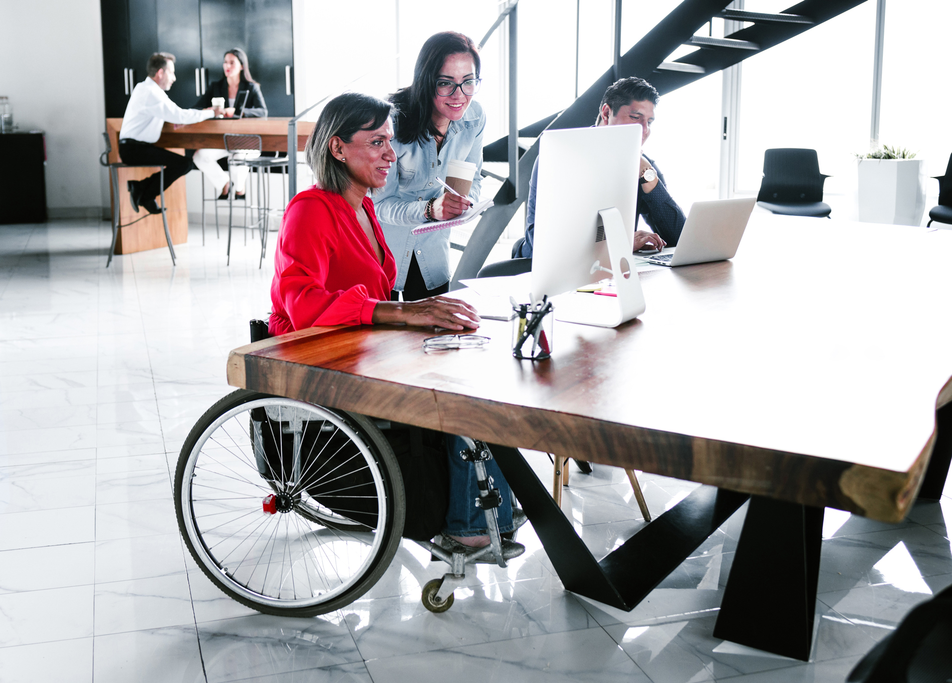 A colleague in a wheelchair meets with a colleague before a desktop computer