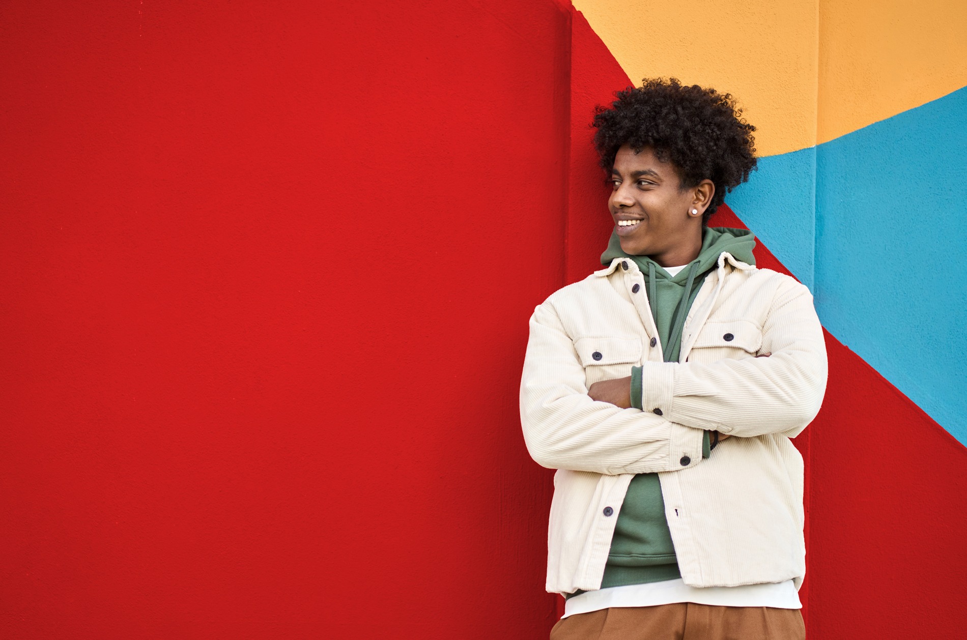 A man looks to the side, smiling and leaning against a colorful and simple backdrop.
