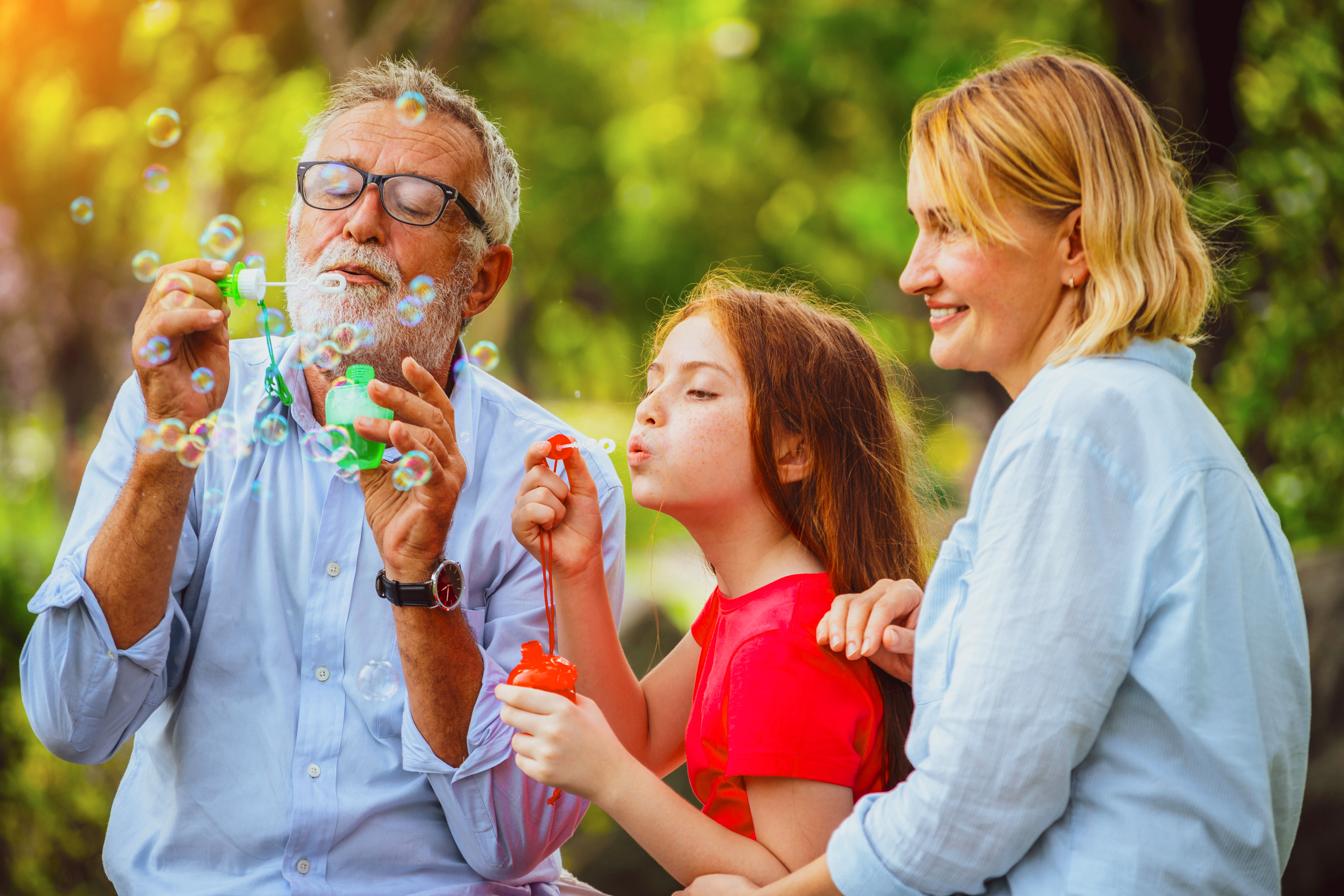 A grandfather blowing bubbles with his grandchild and daughter