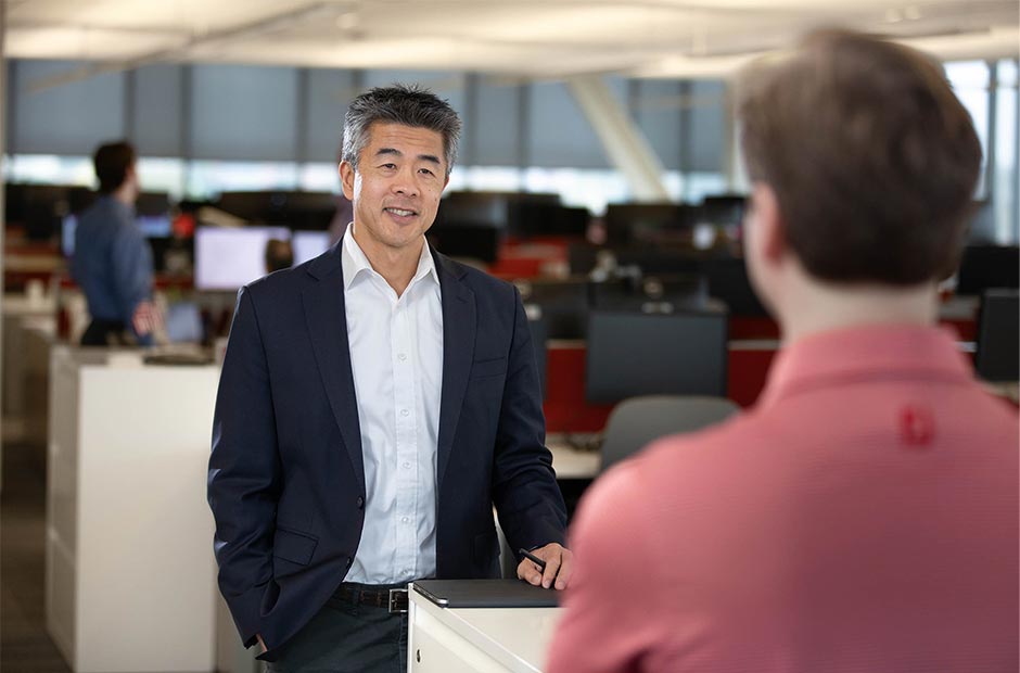Howard Liao engaged in a discussion at the RGA headquarters with multiple computer workstations and large windows in the background.