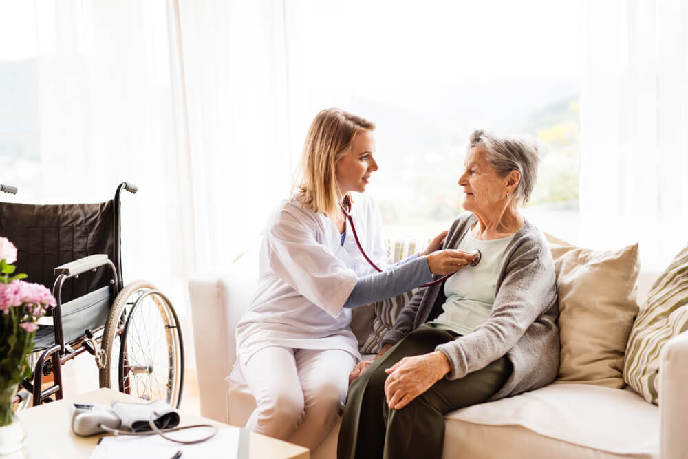 A home healthcare nurse places a stethoscope on the chest of an elderly patient