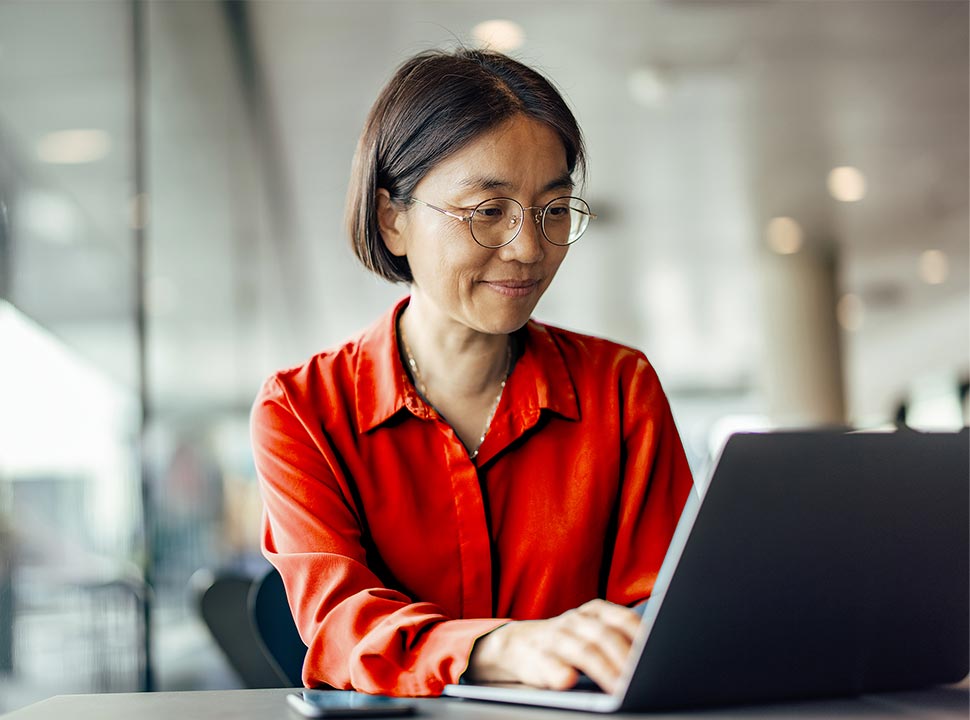 Asian Woman in a Red Shirt Looking at a Laptop Screen