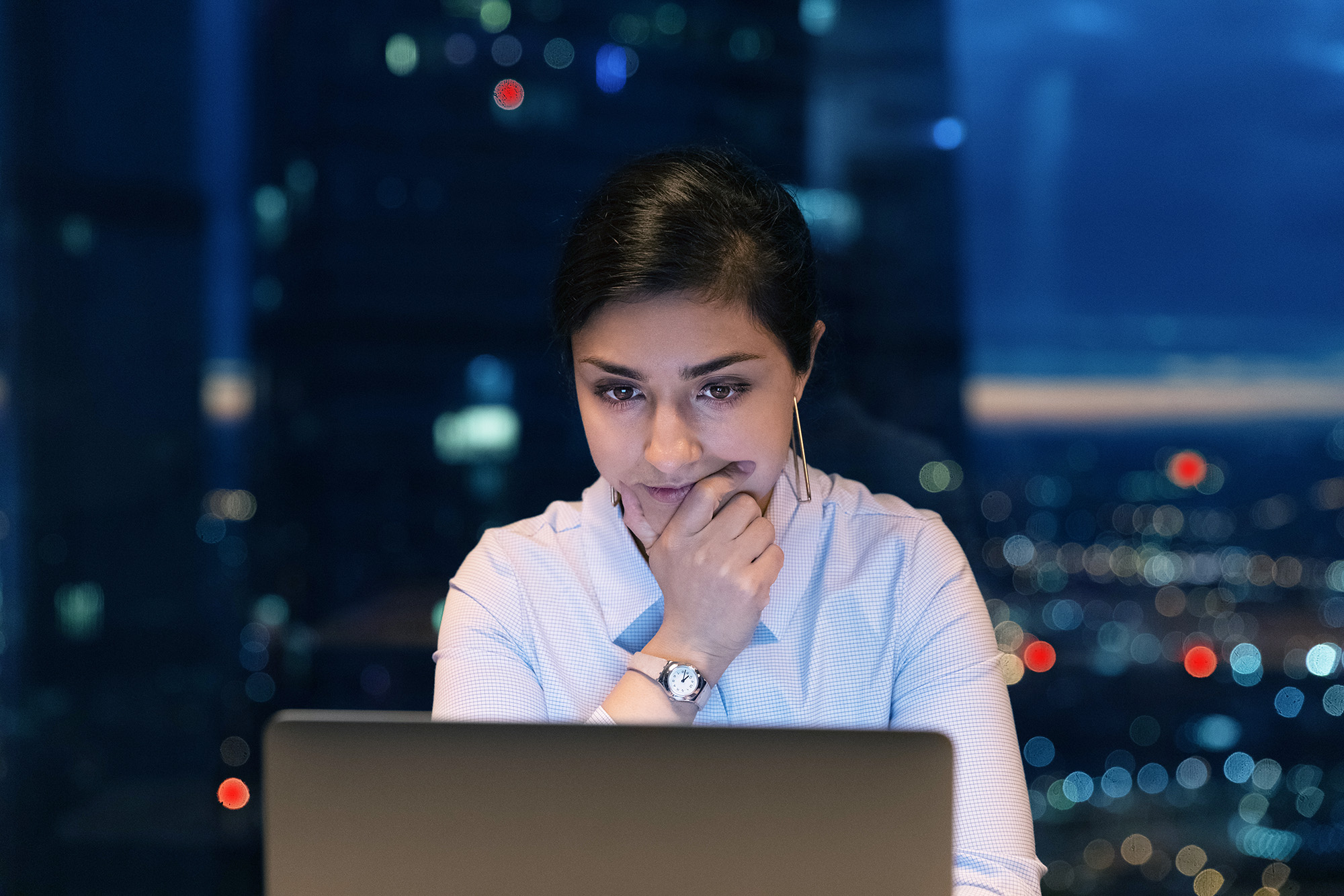 Woman in an office with large windows looking at her laptop