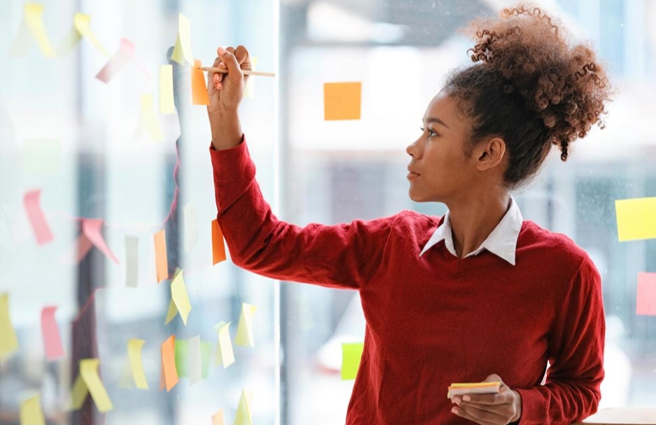 Woman in red shirt scribbles post-it notes on a glass wall