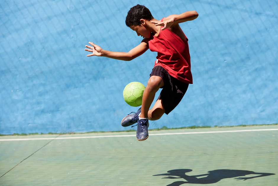 A boy leaps and kicks a ball