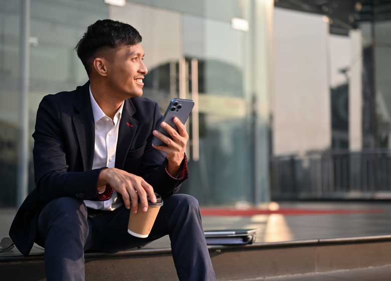 A man holds a smartphone as he gazes ahead into the distance and smiles