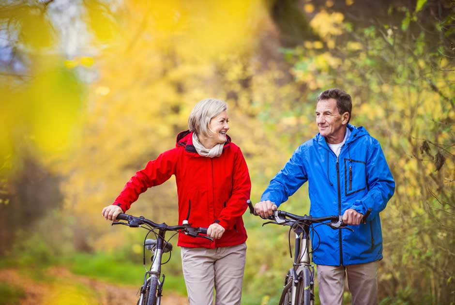 An older couple walk their bikes down a wooded path