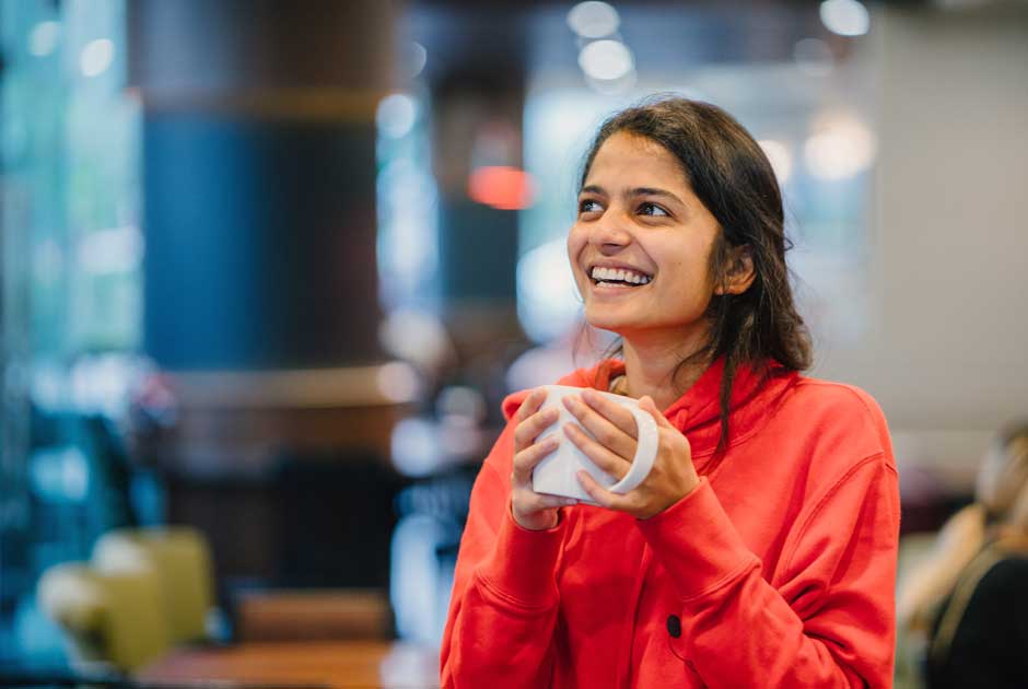 A woman smiles in conversation while clutching a coffee mug